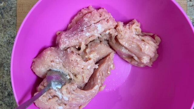 Adding salt to raw ground chicken in a bowl to make frikadelles. Top view.