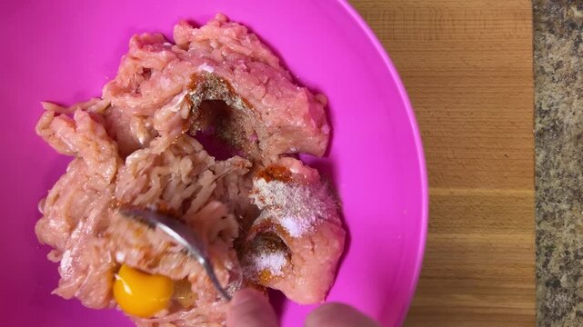 Mixing raw minced chicken with raw chicken egg, salt and spices. The process of making chicken frikadelles. Top view.