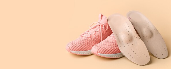 Orthopedic insoles and sneakers on beige background with space for text