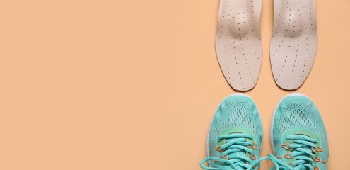 Pair of sneakers and orthopedic insoles on beige background with space for text