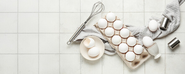 Cardboard holder and bowl with raw chicken eggs on white tile background