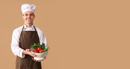 Happy male chef holding colander with fresh vegetables on brown background with space for text