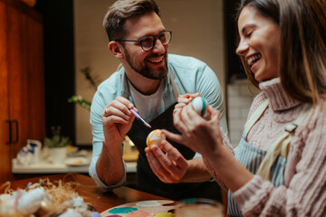 Young couple enjoying easter egg painting activity together at home