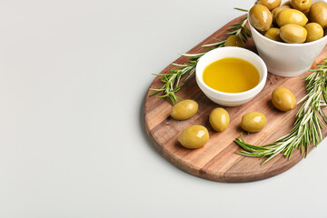 Bowls with ripe olives and oil on grey background