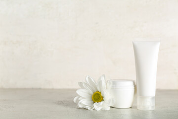 Cosmetic products and chamomile flower on table against light background