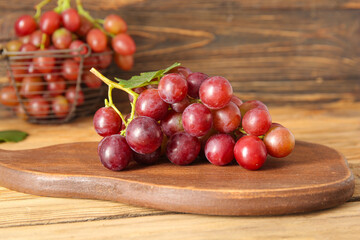 Board with tasty ripe grapes on wooden background