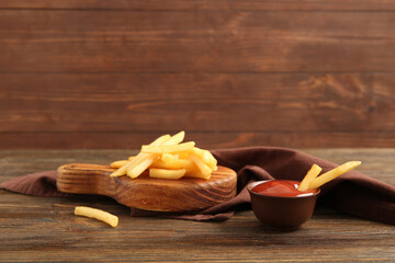 Board with tasty french fries and bowl of ketchup on brown wooden background