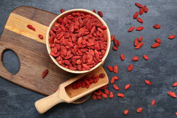 Bowl and scoop with red dried goji berries on black background