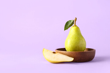 Bowl with ripe pear and cut piece on lilac background