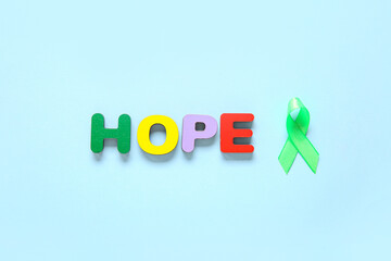 Green awareness ribbon and word HOPE made of wooden letters on blue background. Mental Health Day