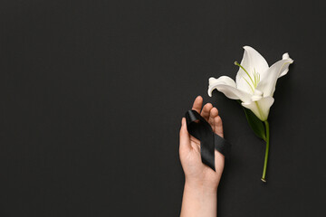 Female hand with ribbon and lily flower on black background