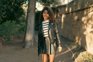 Fototapeta premium Young woman walking in a park wearing leather jacket and skirt