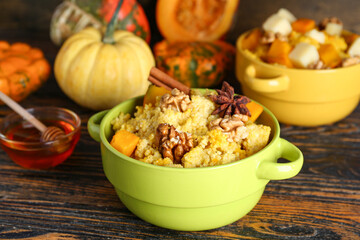 Pot of tasty millet porridge with pumpkin on wooden background