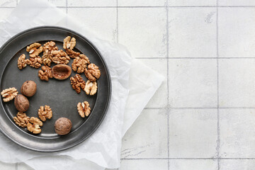 Plate of tasty walnuts on white tile background