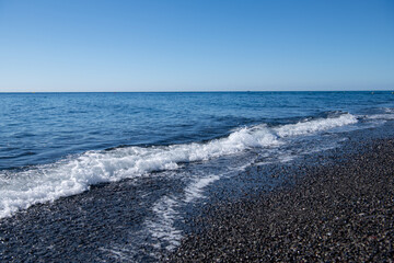 Slowly sea waves on the coastline of Santorini, black sand and blue water