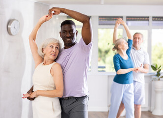 Active mature men and women practicing Ballroom dances in training hall during dancing classes