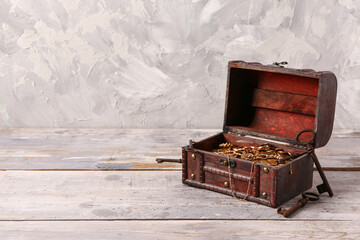 Old chest with treasures and keys on light wooden table near grunge wall