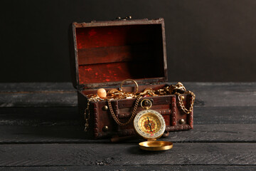 Old chest with treasures and compass on brown wooden table near black wall
