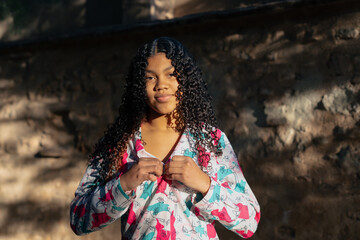 Fototapeta premium Young latin girl adjusting her colorful shirt in front of a stone wall