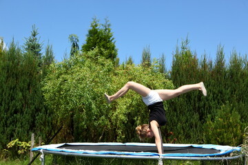 A young girl joyfully performing an impressive handstand on a trampoline in a sunny backyard