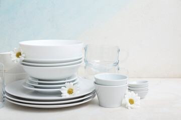 Composition with clean dishes, cups and beautiful chamomiles on table near light wall