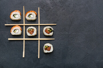 Game of Tic-tac-toe with tasty sushi rolls and chopsticks on black grunge background
