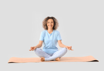 Sporty mature woman meditating on yoga mat against light background