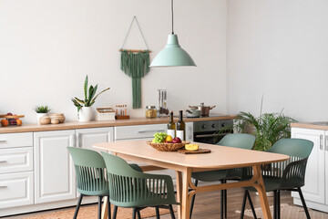Interior of modern kitchen with dining table, chairs, white counters and lamp