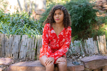 Naklejka premium Young woman sitting in a garden wearing a red floral playsuit