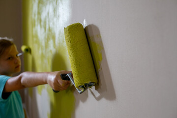 A child joyfully painting a wall with a bright green roller, showcasing creativity and fun