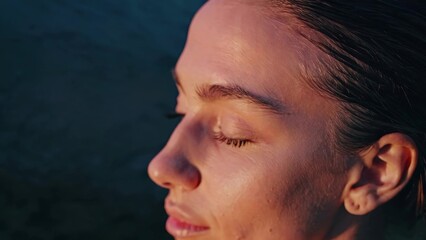 Close-up profile of a young woman with wet hair, closing her eyes and enjoying the warm light of the sunset, conveying a sense of tranquility and serenity