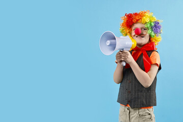 Happy little boy dressed like clown with megaphone on light blue background, space for text....
