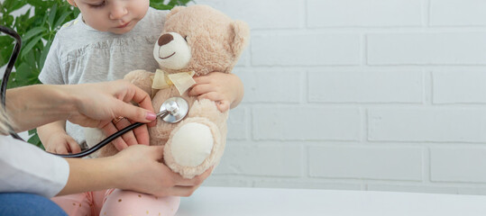 Female doctor examining little girl, listening to lungs with stethoscope. Pediatrician's appointment