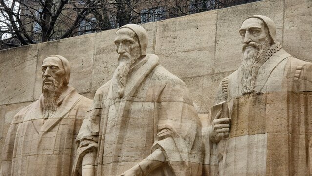 A close-up of the Reformation Wall in Geneva, Switzerland, featuring statues of Protestant Reformation leaders, including John Calvin, William Farel, and Theodore Beza.
