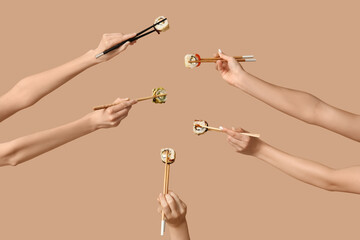 Female hands holding chopsticks with different tasty sushi rolls on beige background