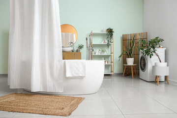 Bathtub with curtain, rack and folding screen in interior of light bathroom