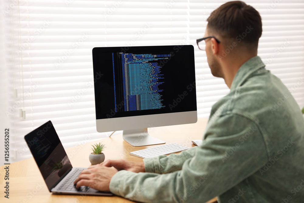 Aufkleber programmer working on laptop and computer at wooden desk indoors