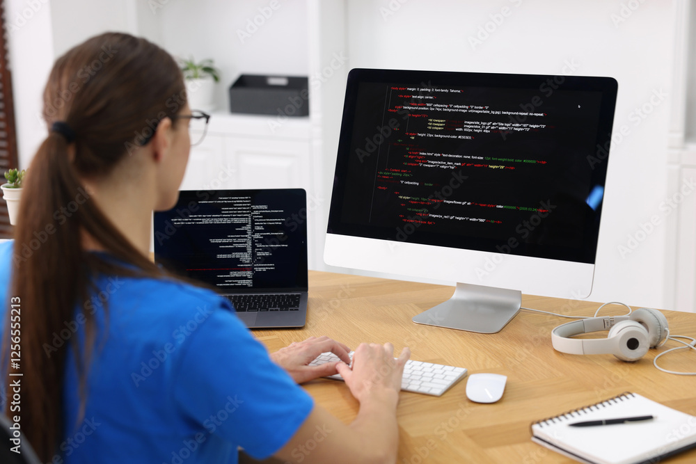 Poster programmer working on laptop and computer at wooden desk indoors, back view