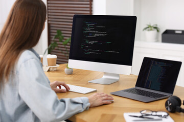 Programmer working on laptop and computer at wooden desk indoors, back view