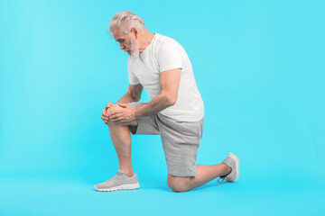 Senior man suffering from pain in his knee on light blue background