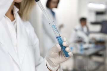 Scientist with micropipette and test tube working in laboratory, closeup