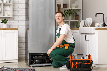 Happy male worker of repair service with tools near fridge sitting in kitchen