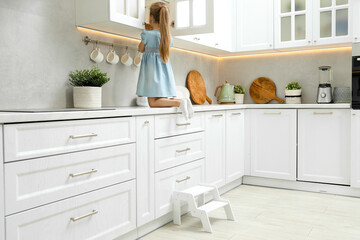 Little girl sitting on counter near step stool in kitchen