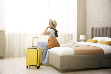 Traveller with suitcase sitting on bed in hotel room