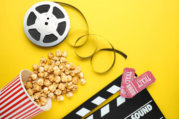 Movie clapper, sweet popcorn, tickets and film reel on yellow background, flat lay