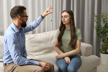 Psychologist using pendulum while working with patient during hypnosis session indoors