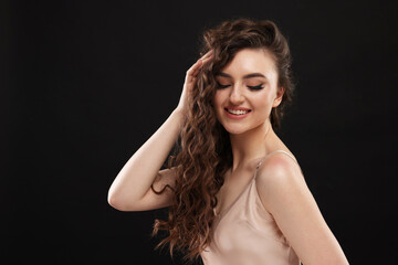 Obraz premium Beautiful young woman with long curly brown hair on black background, space for text