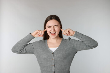 Distressed woman covering her ears from loud noise on light grey background