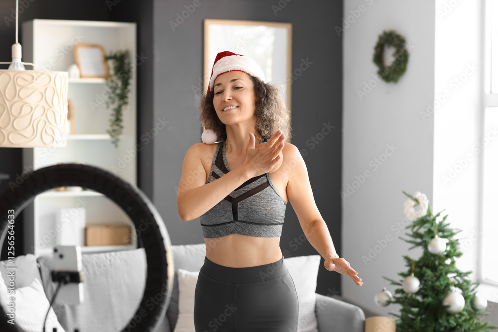 Wall mural Sporty mature woman in Santa hat with massage ball recording video at home on Christmas eve