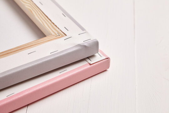 Close-up of the backside of two stacked photo canvas prints, one pink and one gray, showcasing tightly stretched corners, staple details, and wooden frames on a white surface